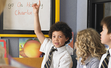 young student holding hand up to answer spelling test question